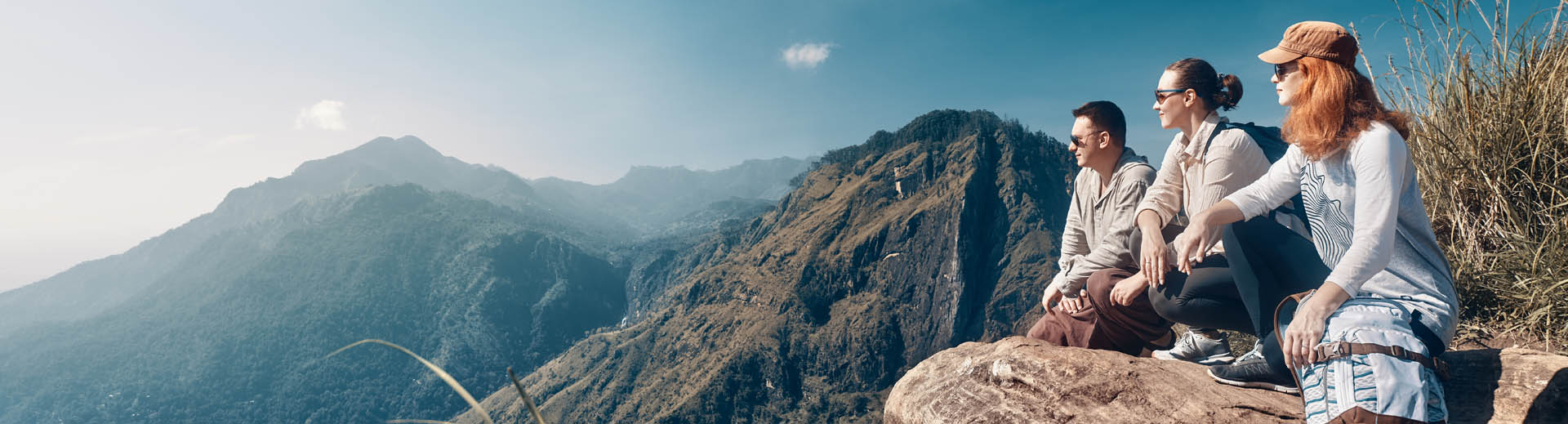 Deux femmes et un homme regardent au loin depuis le sommet d'une montagne