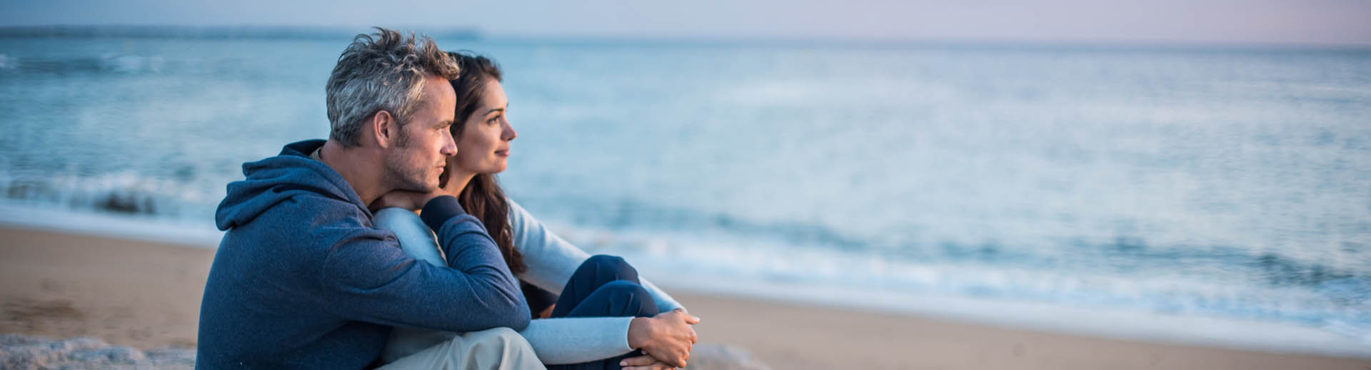 Pärchen sitzt am Strand und schaut auf das Meer