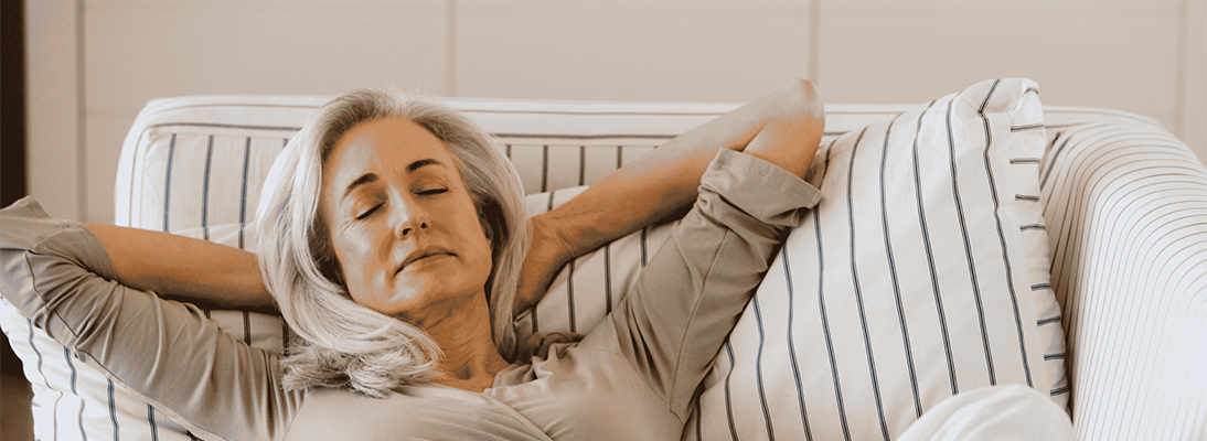 Femme ménopausée détendue, allongée sur le canapé.